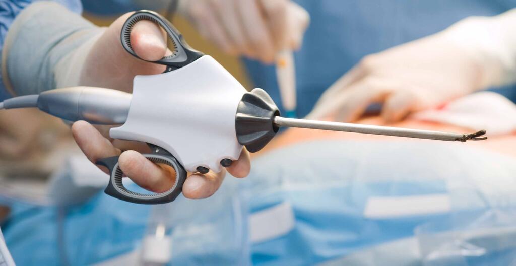 A hand holding an ultrasonic surgical tool with an operation occurring in the background