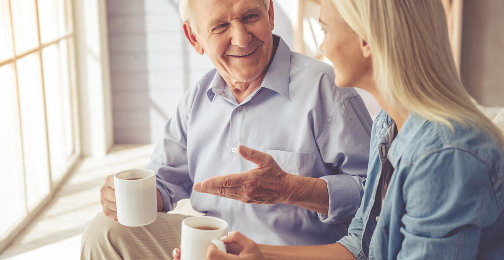 An elderly man and a younger woman having a talk over a hot beverage