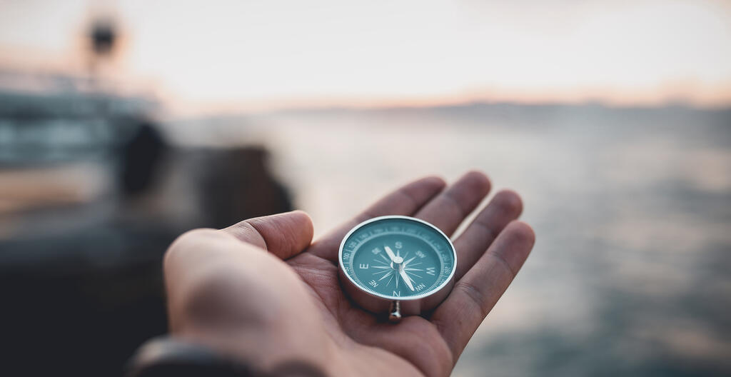 A palm holding a compass with a blurred out ocean background