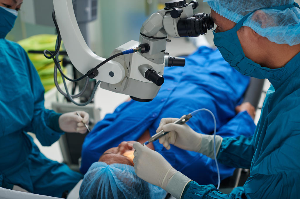Two surgeons in surgical gear conducting cataract surgery on a patient