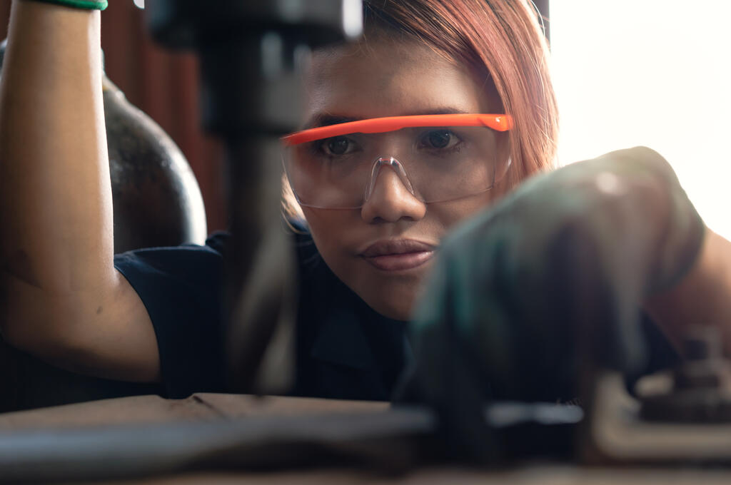 A woman wearing safety goggles and working with a drill in an R&D department.