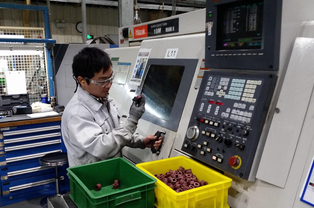 A shopfloor worker inspecting polymer components next to a CNC machine