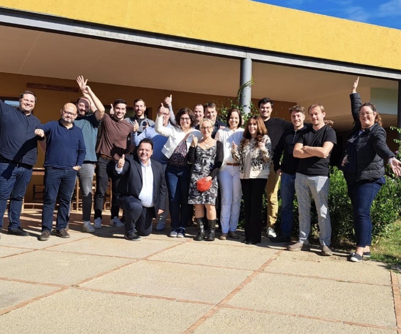 A diverse group of people from Omniseal Solutions stands together in front of a large building, smiling and engaging with one another.