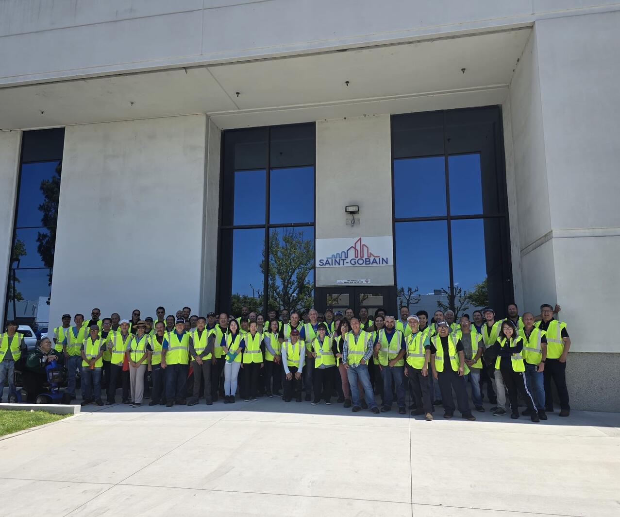 Large group of Omniseal Solutions Production Operators in yellow high-vis vests standing in front of a Saint-Gobain building.