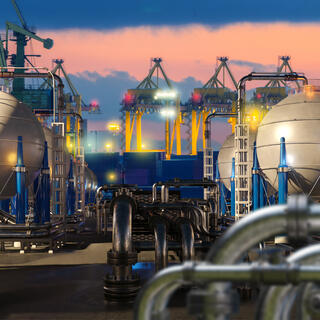 Liquefied natural gas terminal with spherical storage tanks, pipelines and cranes at port during sunset operations. LNG storage, transport, energy industry