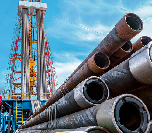 A number of large pipes with an oil derrick in the background