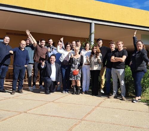 A diverse group of people from Omniseal Solutions stands together in front of a large building, smiling and engaging with one another.