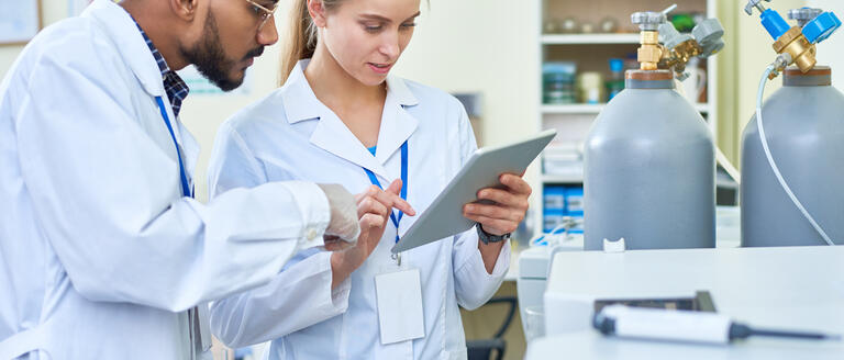A man and woman in labwear, looking at a tablet in a lab setting