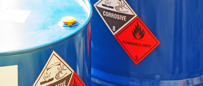 Two blue barrels with visible corrosion and flammability labels, positioned side by side against a neutral background.